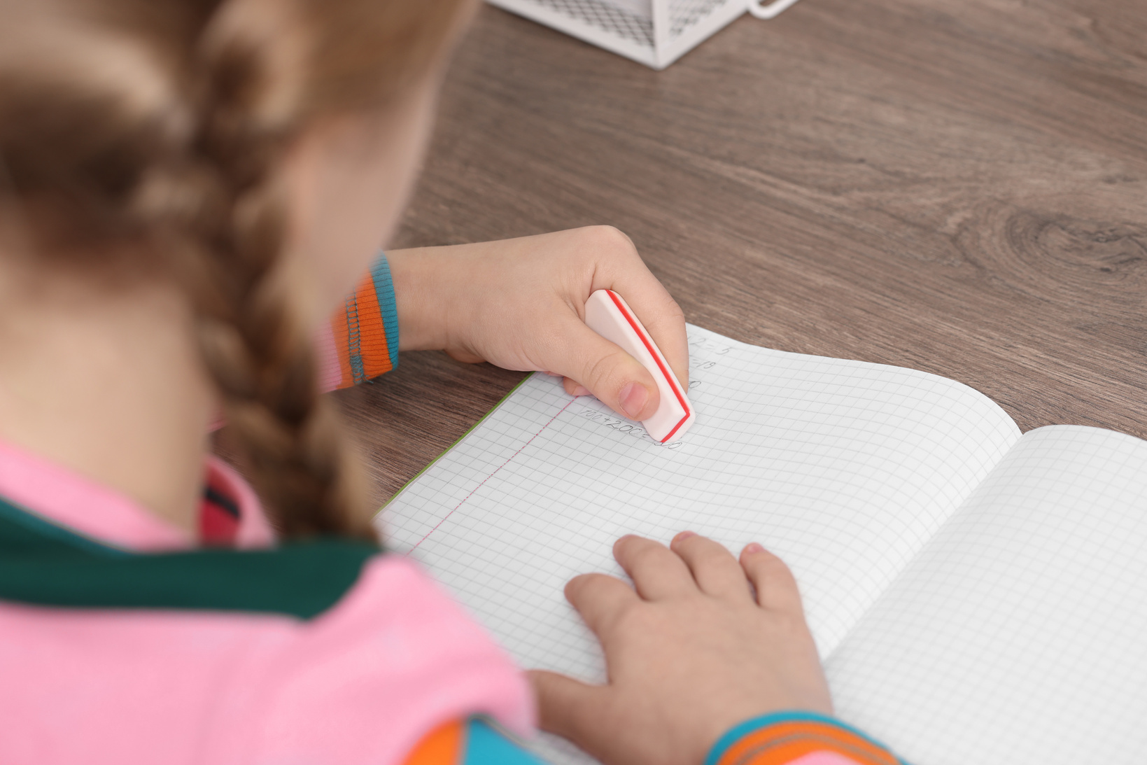 Girl erasing mistake in her homework at wooden table, closeup